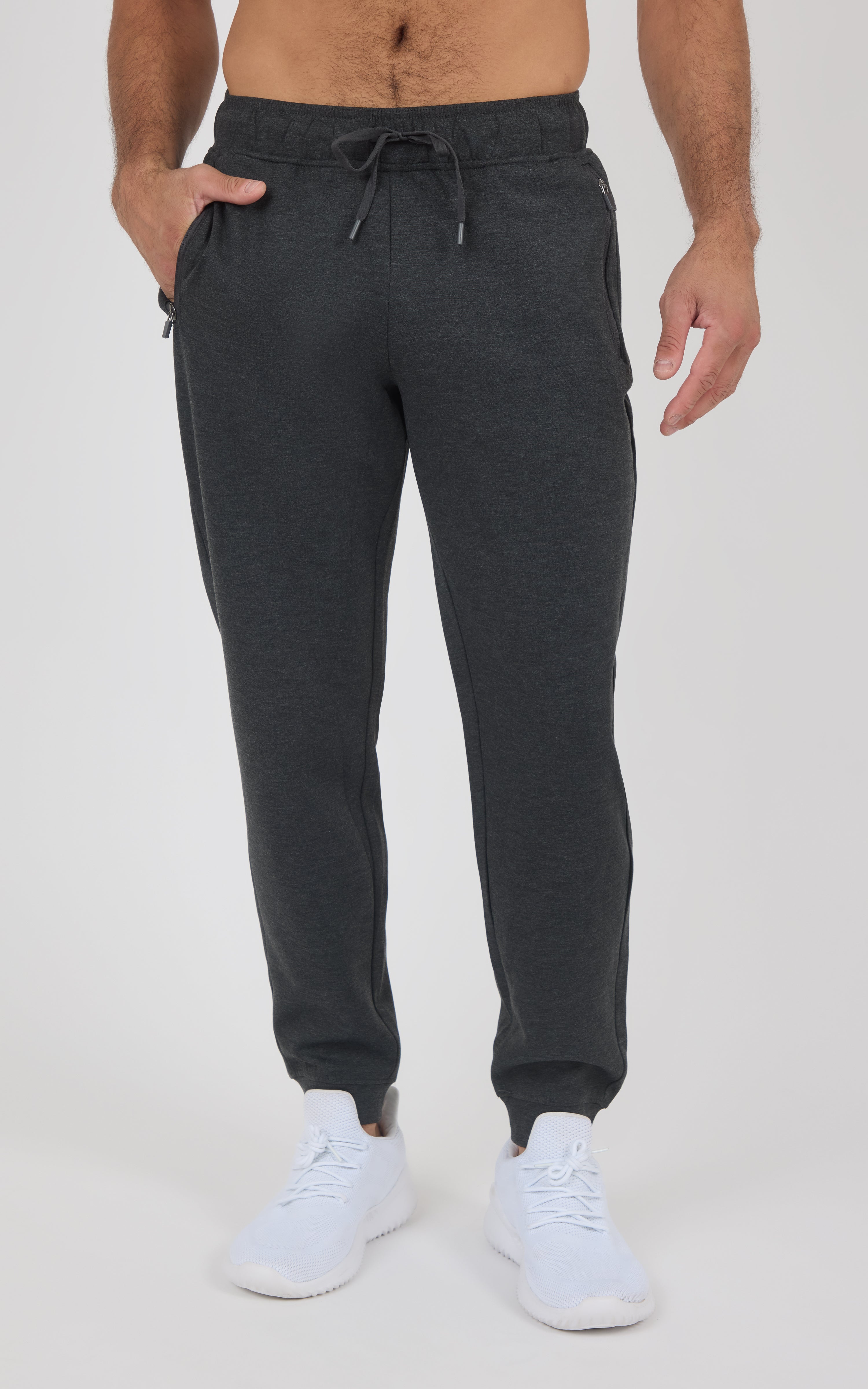 Dark charcoal men’s jogger pants with a drawstring waist, tapered legs, and elastic cuffs, paired with white sneakers.