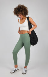 Light green slim-fit joggers with interlock zipper pockets, worn with white crop top and black woven shoulder bag.