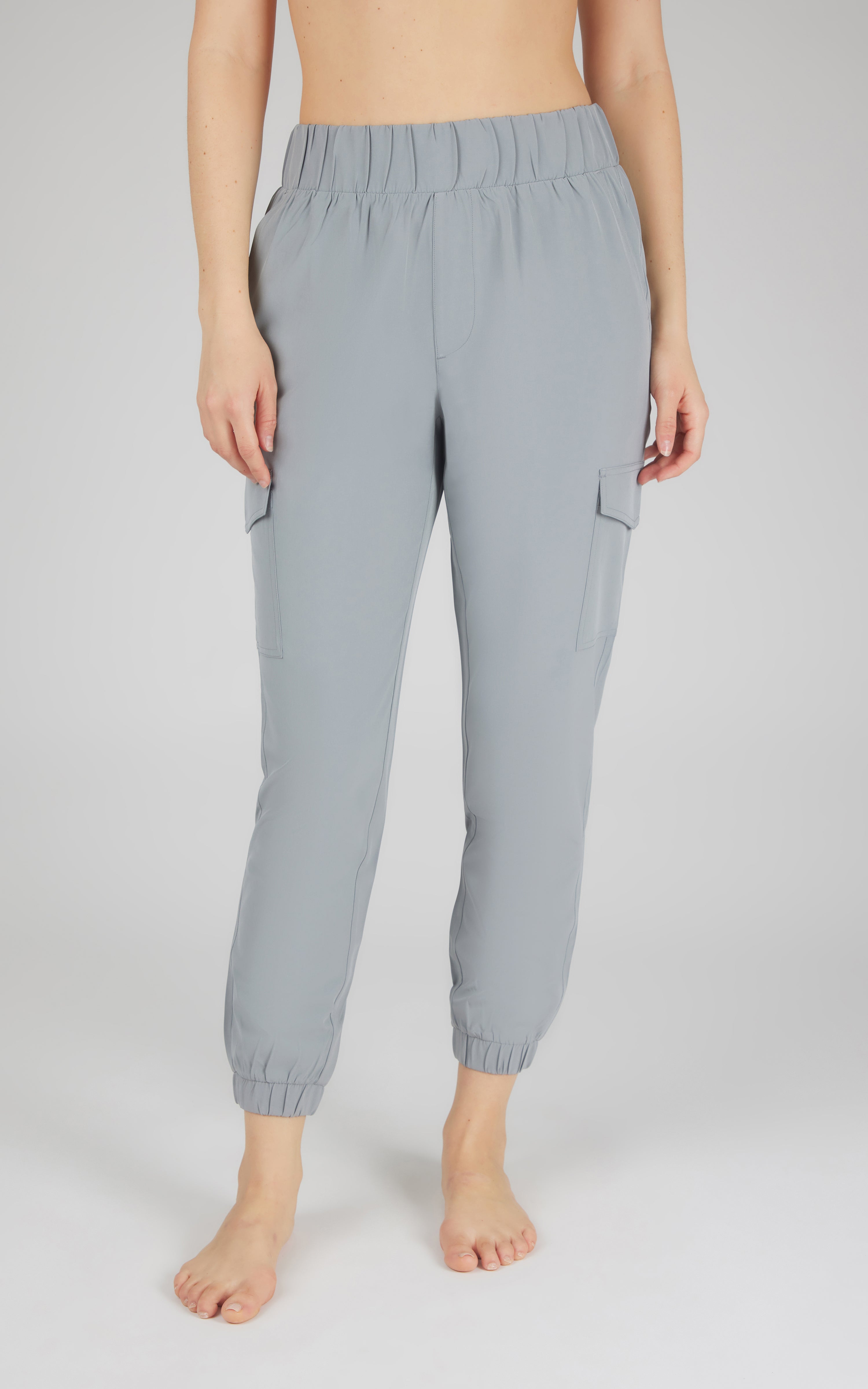 Light grey cargo joggers with side pockets and elastic waist and cuffs on a barefoot model.