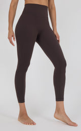 A model wearing high-waisted, ankle-length leggings in a solid dark brown color, shown from the waist down against a light gray studio background.