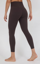 A model shown from the back wearing dark brown high-waisted leggings, standing barefoot against a light gray studio background.