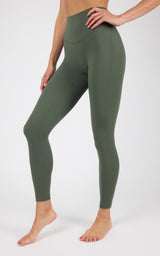 A model wearing high-waisted, full-length leggings in a muted olive green color, shown from the waist down.