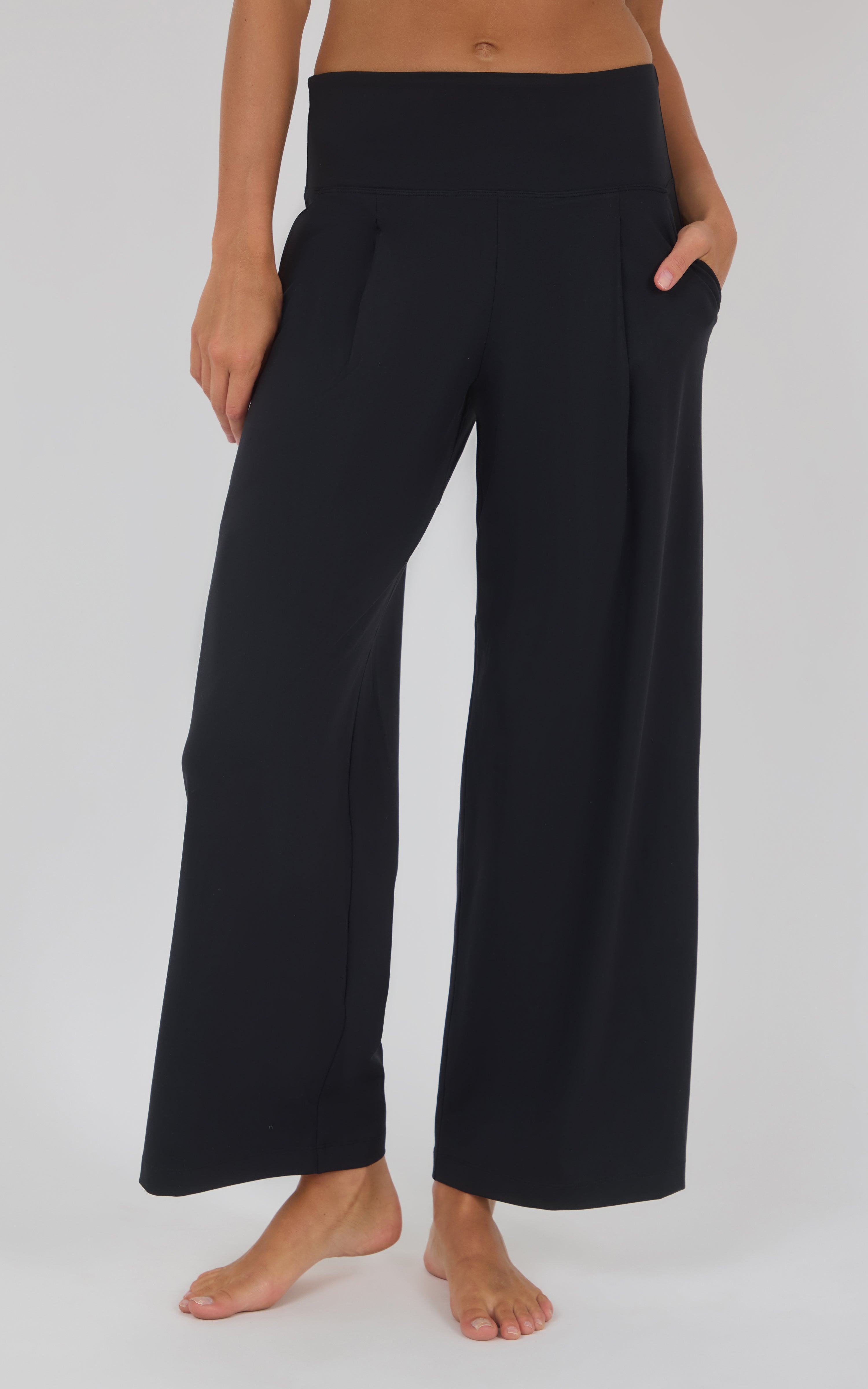 Black high-waisted wide-leg trousers with a smooth finish, flowing drape, and side pockets.