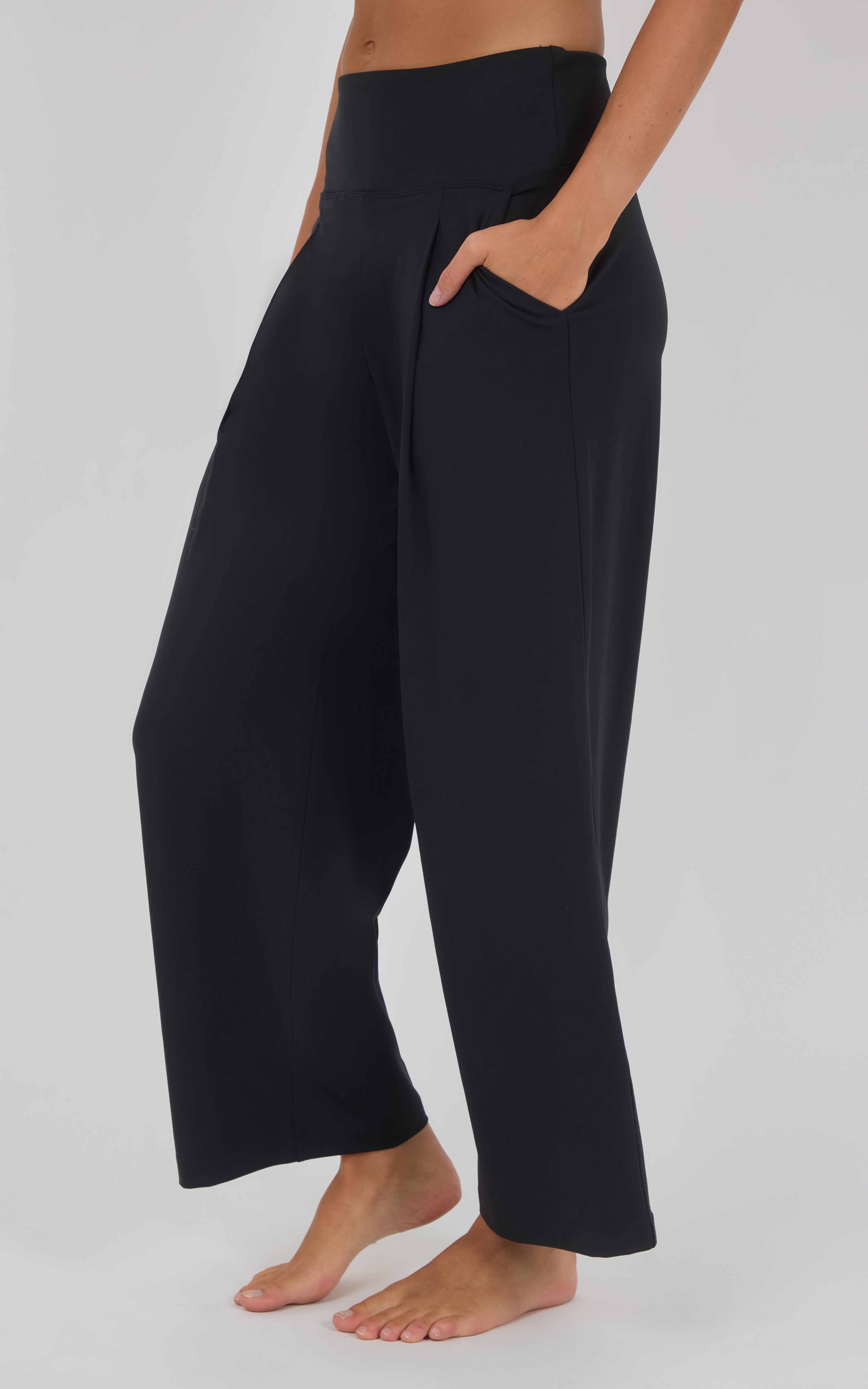 Black high-waisted wide-leg trousers with front pleats, side pockets, and a cropped hem, worn barefoot.