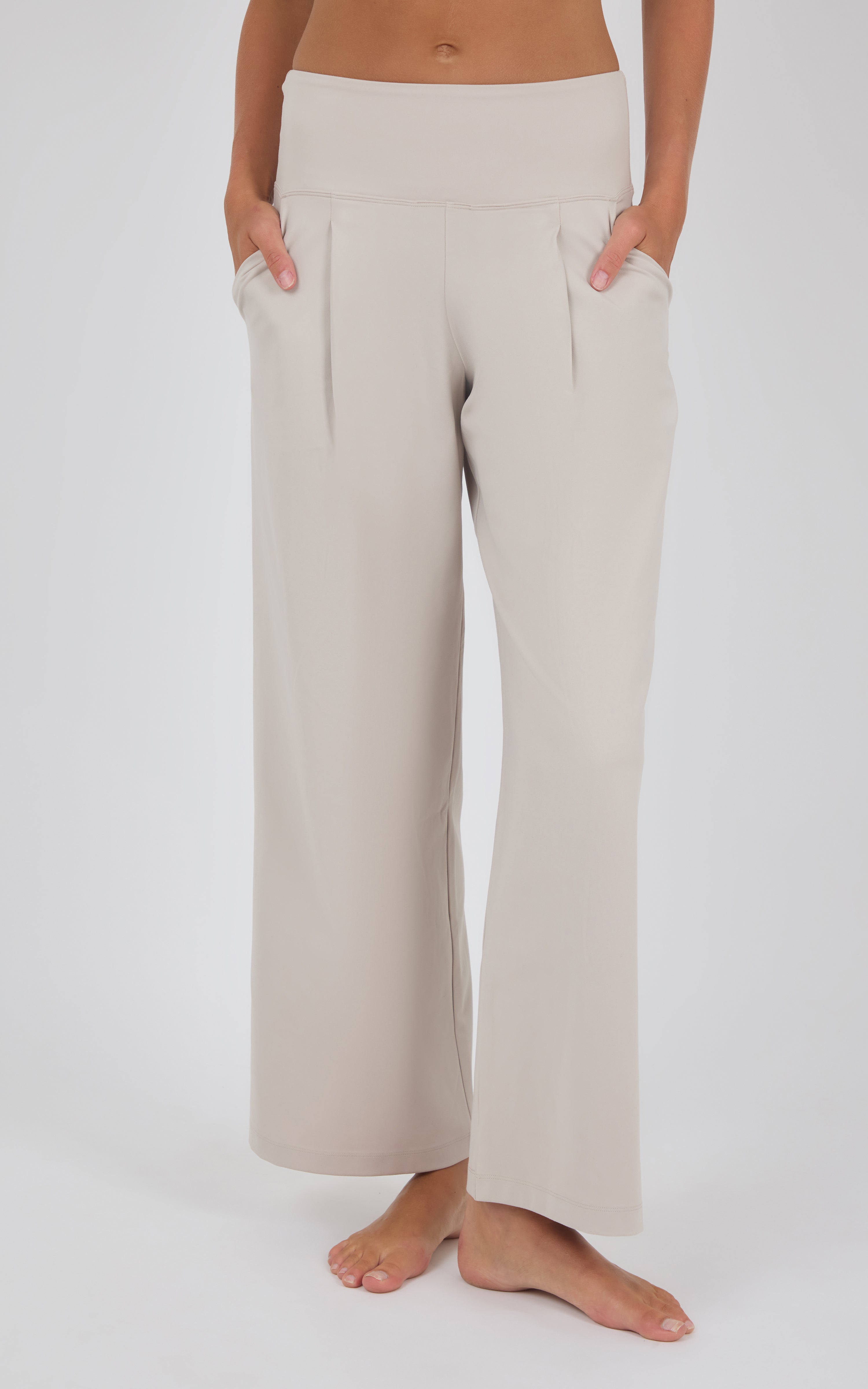Cream high-waisted wide-leg trousers with soft front pleats, shown on a model standing barefoot.
