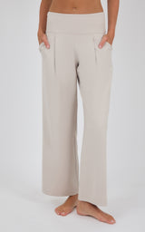 Cream high-waisted wide-leg trousers with soft front pleats, shown on a model standing barefoot.