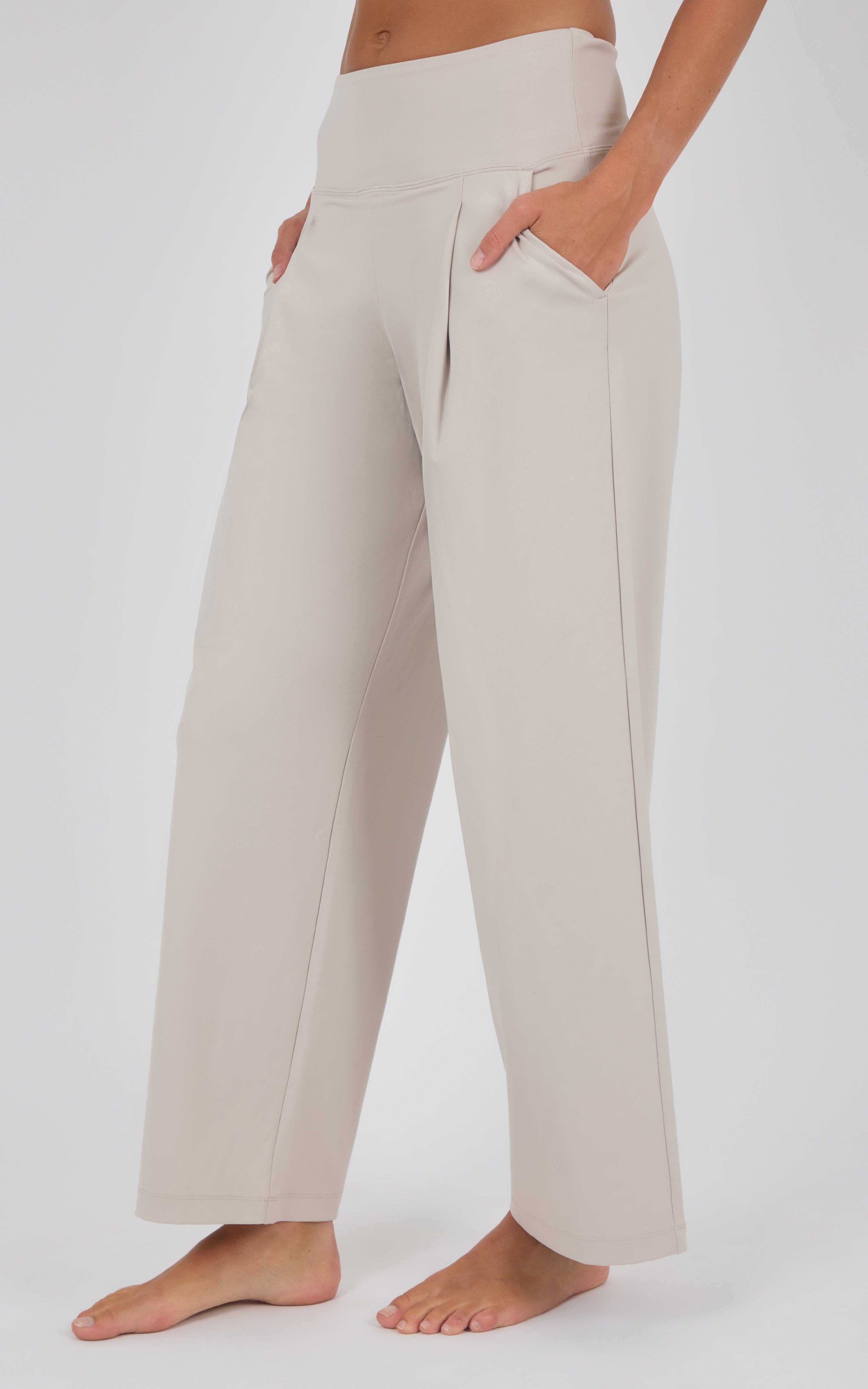 Ivory pleated wide-leg trousers with a high waist and relaxed fit, modeled with bare feet.