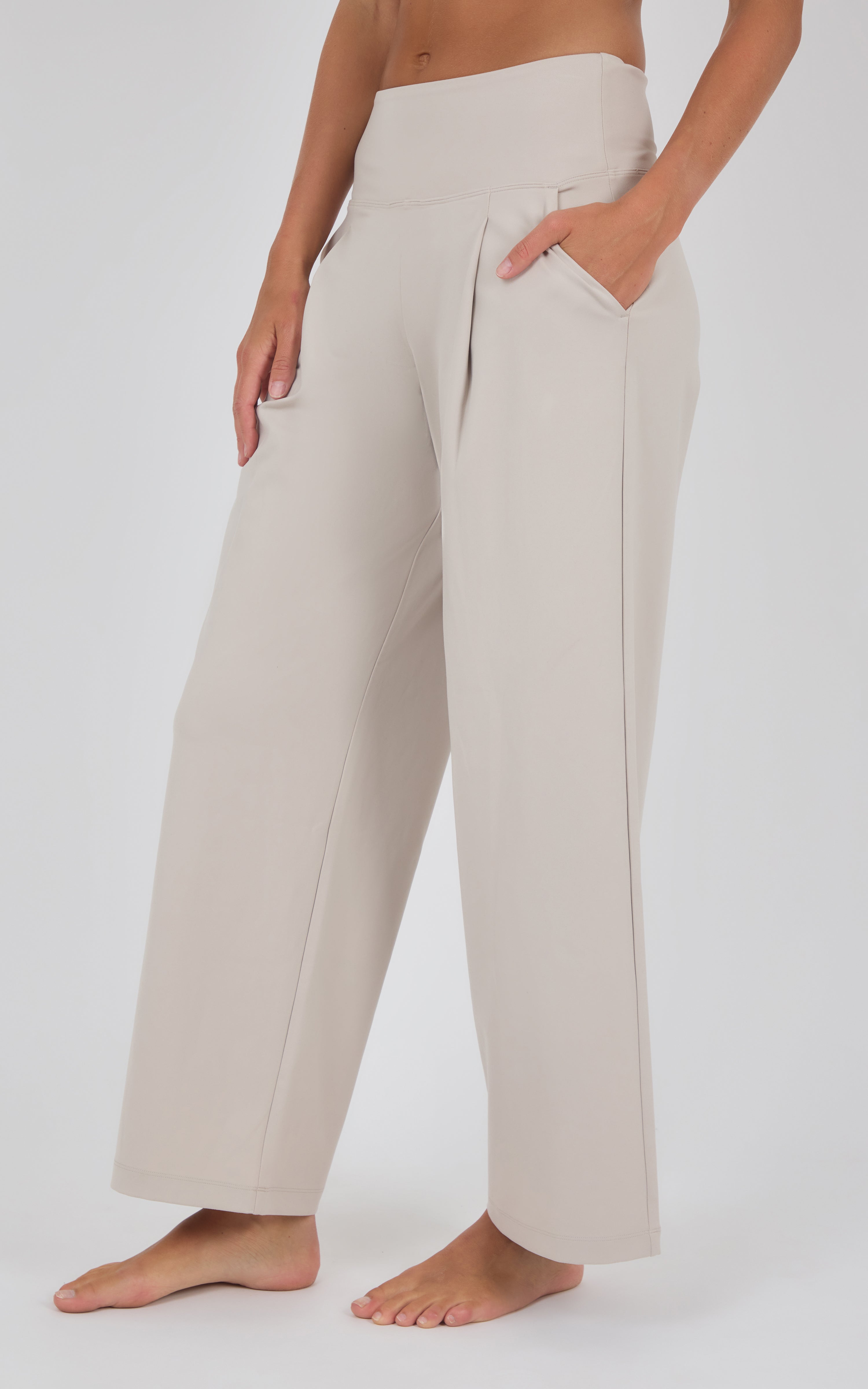 Ivory wide-leg trousers with a high waist, subtle front pleats, and a relaxed drape, shown with a cropped top and bare feet.