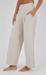 Ivory wide-leg trousers with a high waist, subtle front pleats, and a relaxed drape, shown with a cropped top and bare feet.