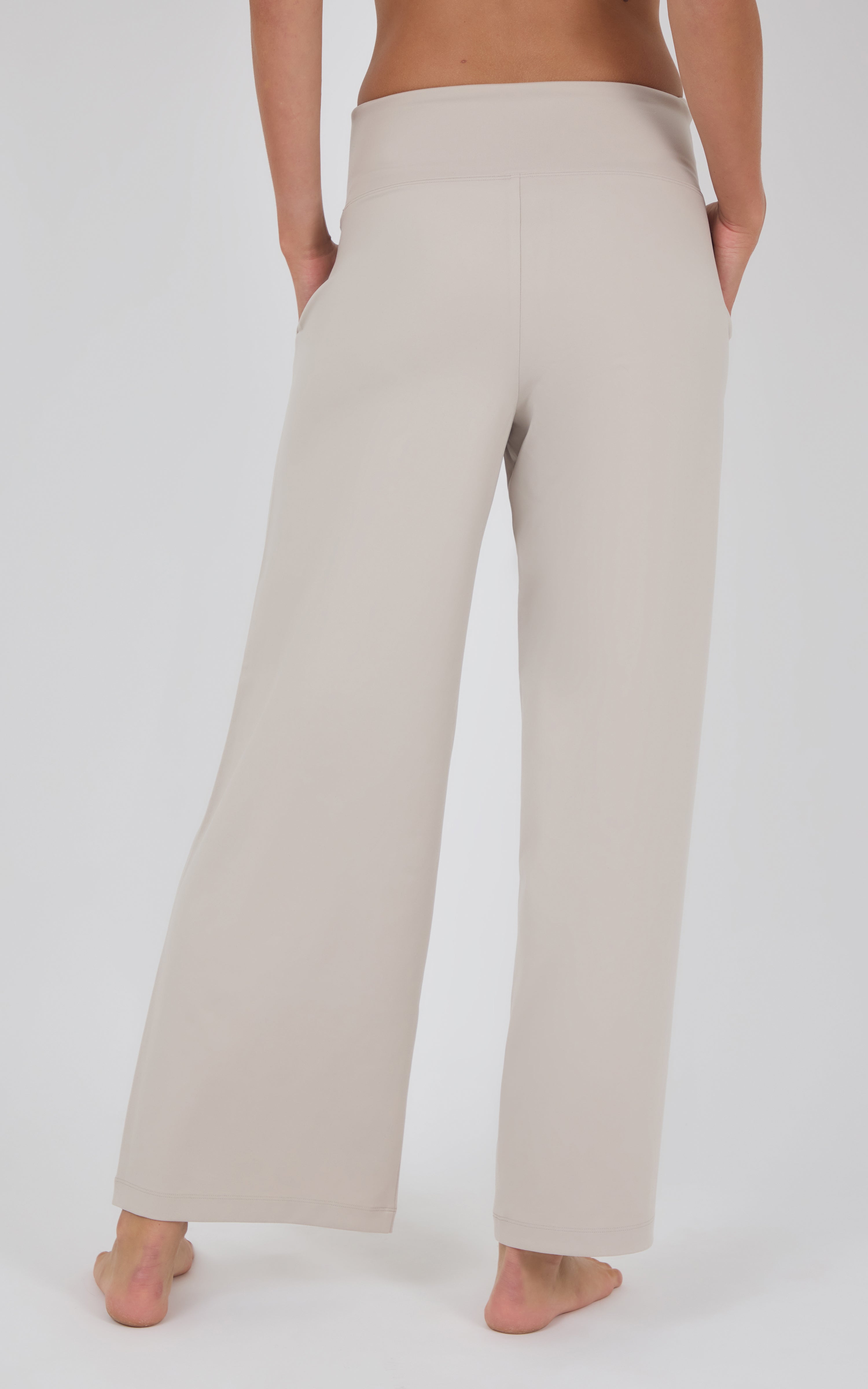 Rear view of cream wide-leg pleated trousers with a high waist and fluid drape, worn with a cropped brown top.