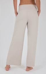 Rear view of cream wide-leg pleated trousers with a high waist and fluid drape, worn with a cropped brown top.