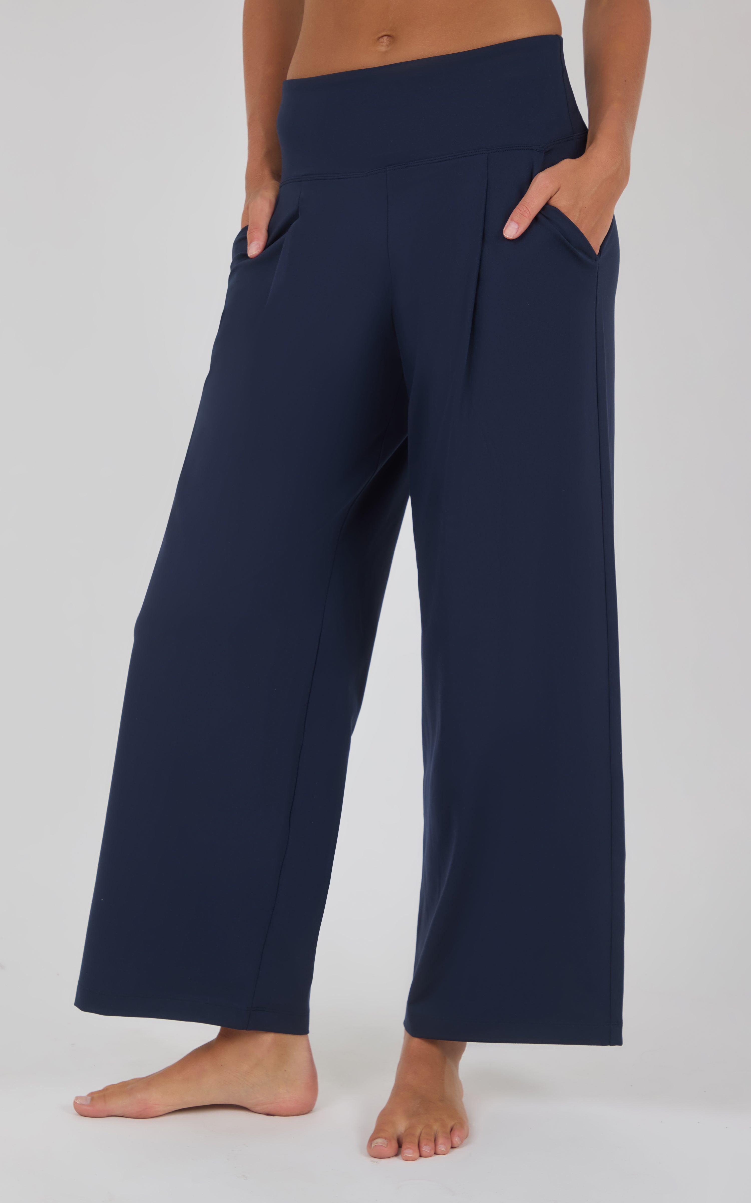 Navy wide-leg pleated trousers with a high waist and flowing cropped hems, modeled barefoot.