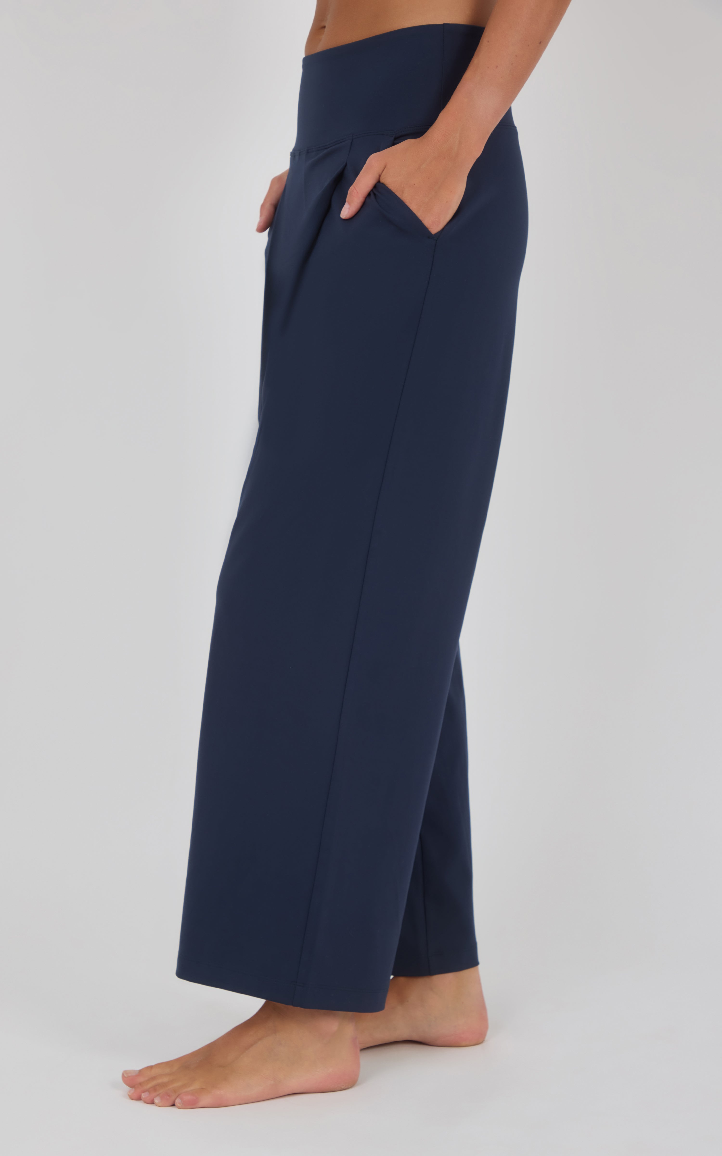 Navy wide-leg pleated trousers with a relaxed drape, shown from the side with a cropped hem above bare ankles.