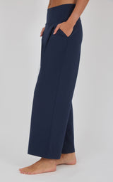 Navy wide-leg pleated trousers with a relaxed drape, shown from the side with a cropped hem above bare ankles.