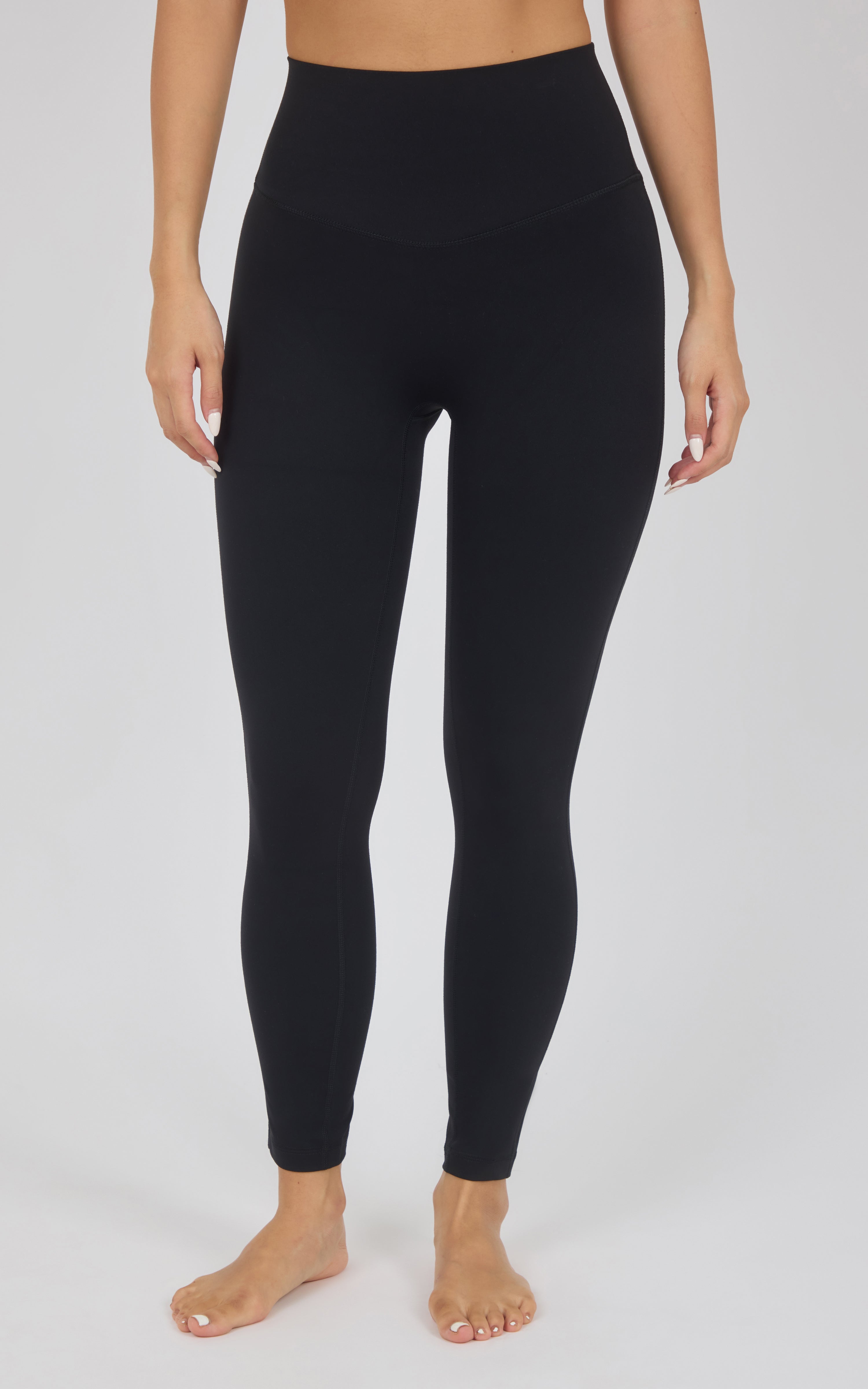 Black high-waisted leggings worn by a model, shown from the waist down against a light gray studio background.