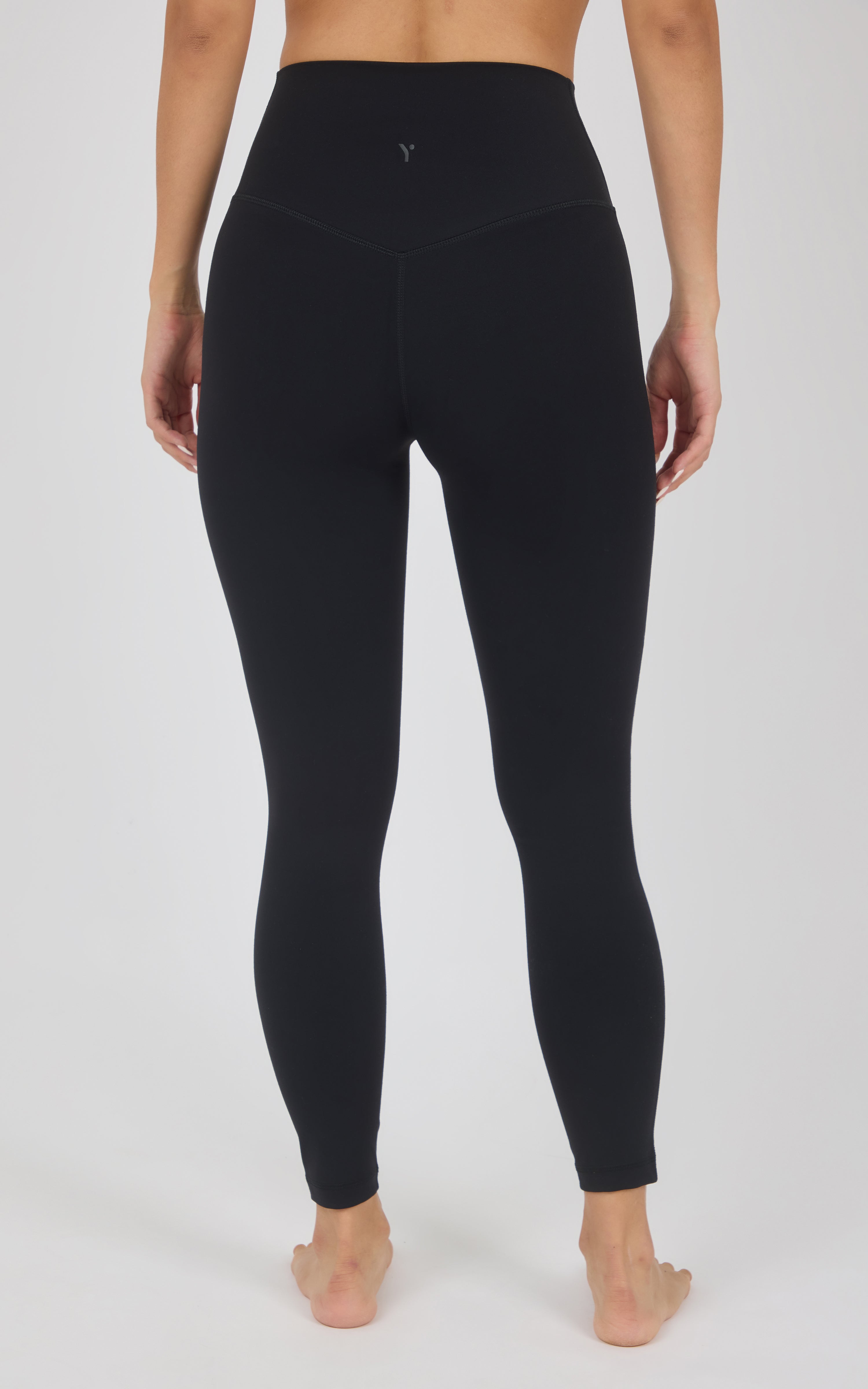 Rear view of a model wearing black high-waisted leggings against a light gray studio background.