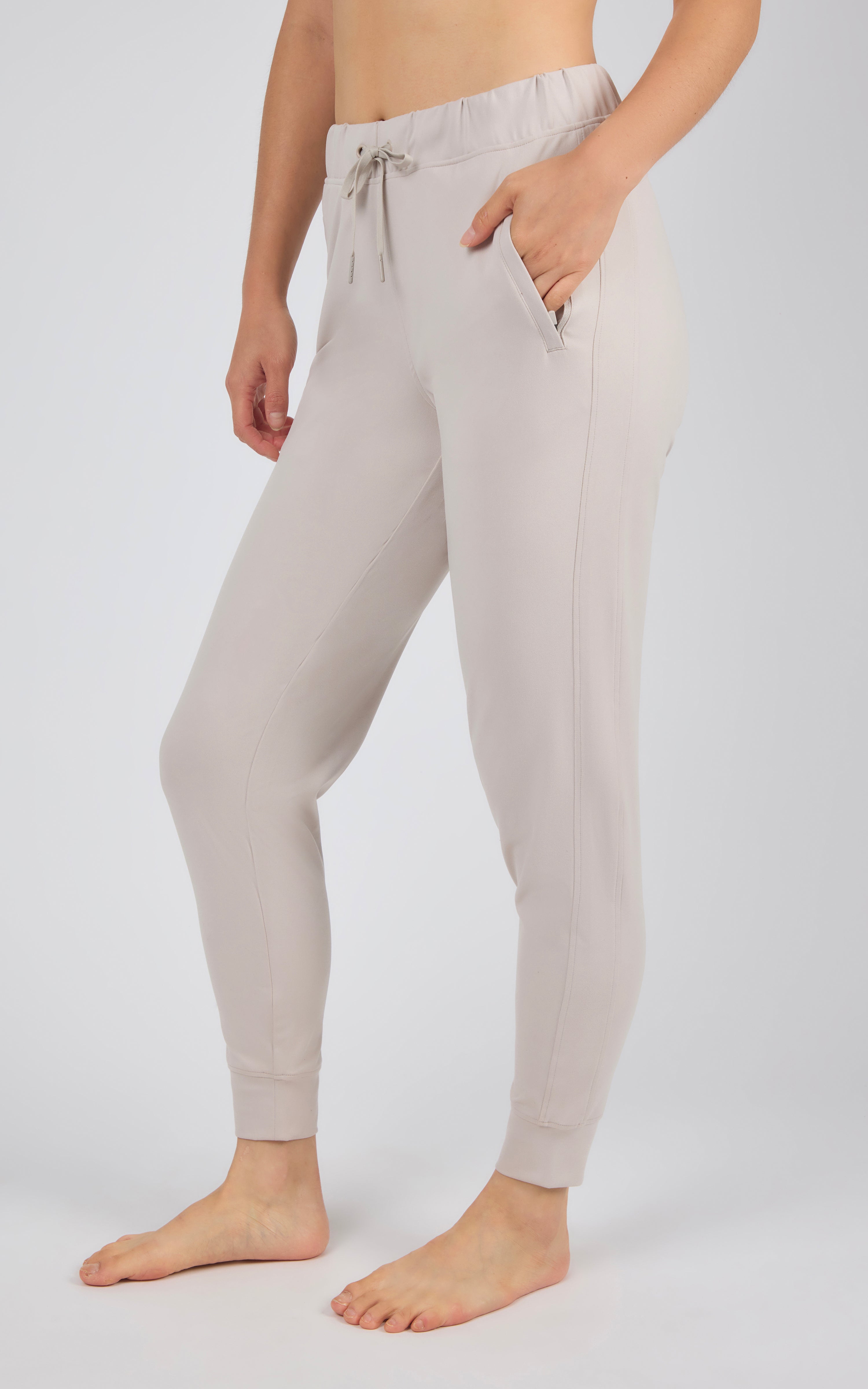 Light gray jogger pants with side pockets, drawstring waist, and ribbed cuffs on a standing model.