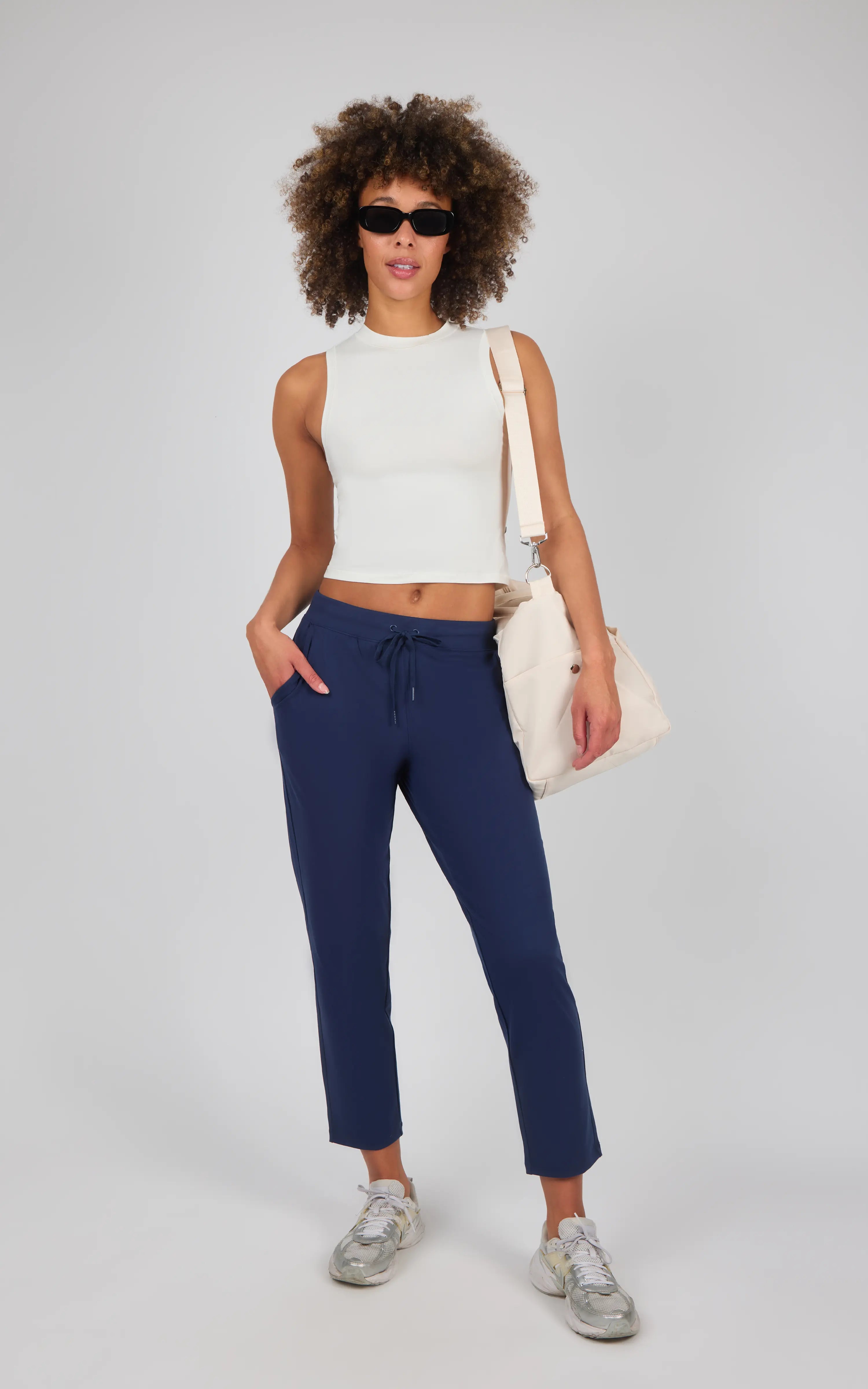 Women's navy straight leg pants with a mid-rise waist and front pockets, styled with a white sleeveless crop top and beige.