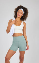 Woman wearing 5-inch high-waisted chino green biker shorts with flat waistband and smooth fabric, paired with white cropped.