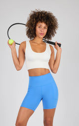 Woman wearing bright blue, 7-inch fitted bike shorts with high waist and smooth fabric, paired with white sleeveless crop.