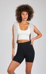 Black high-waisted 7-inch bike shorts with a smooth, fitted design on a woman with curly hair wearing a white cropped tank.