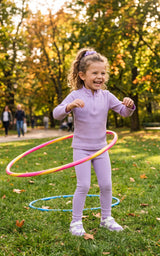 Little girl wearing a lavender half-zip top and matching leggings, jumping rope in a sunny park.