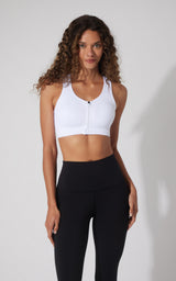 White seamless full zip sports bra with racerback and supportive fit worn with black high-waisted leggings.