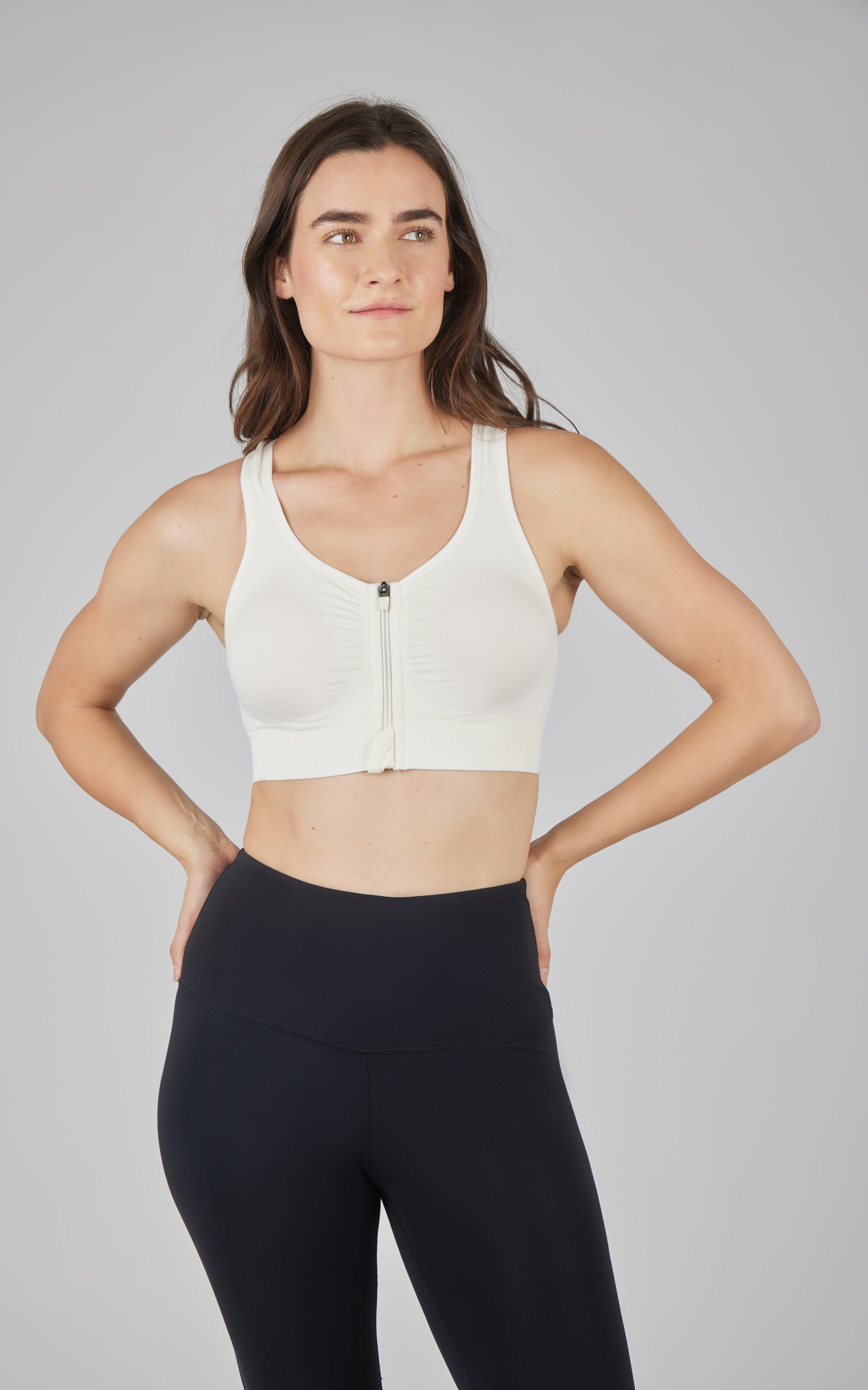Seamless white full zip sports bra with wide straps and supportive band worn with black leggings.