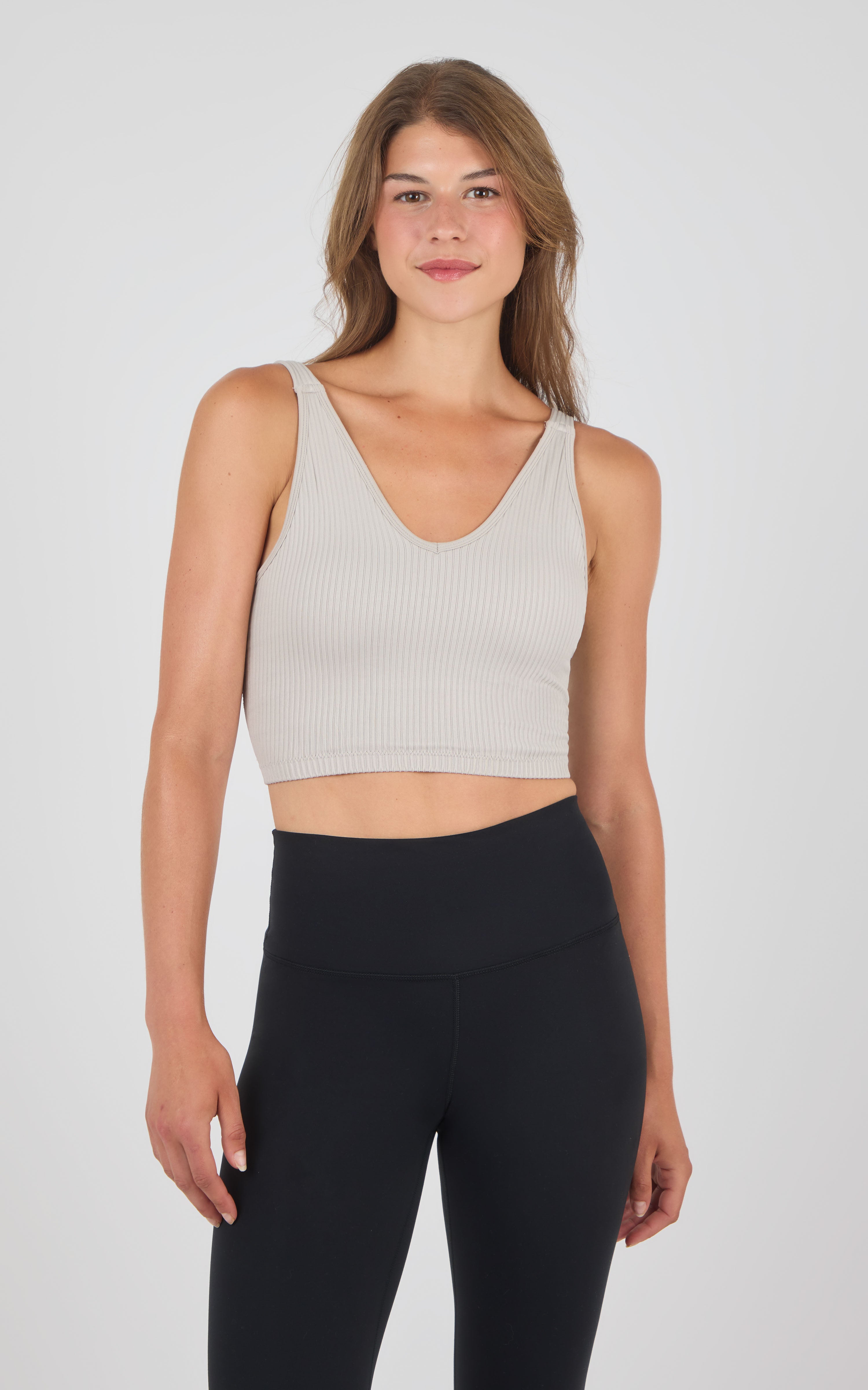 Seamless ribbed crop bra tank in soft beige with V-neck and wide straps, paired with high-waist black leggings.