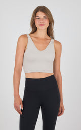Seamless ribbed crop bra tank in soft beige with V-neck and wide straps, paired with high-waist black leggings.