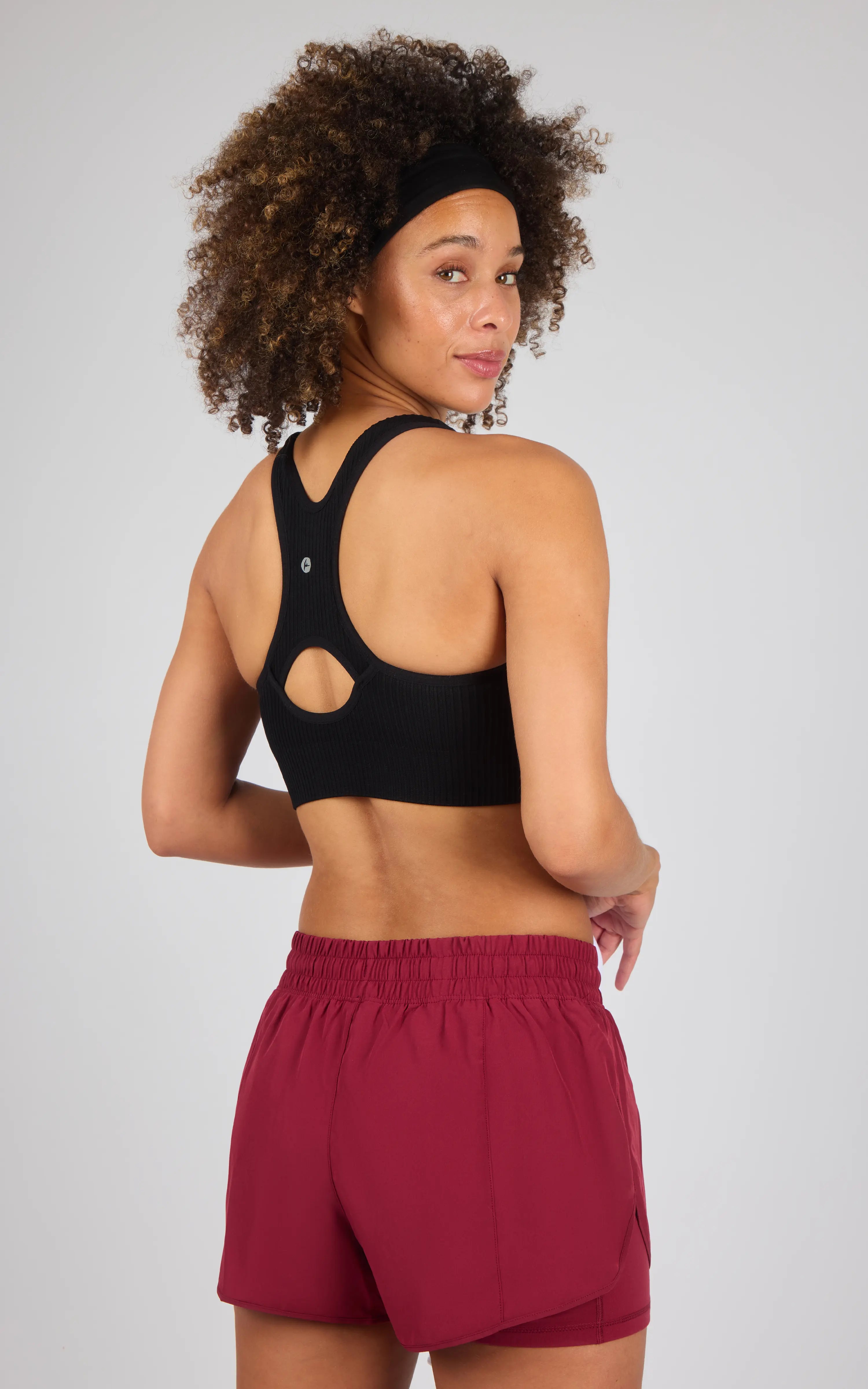 Black seamless textured zip-back sports bra with racerback design worn by woman with curly hair.