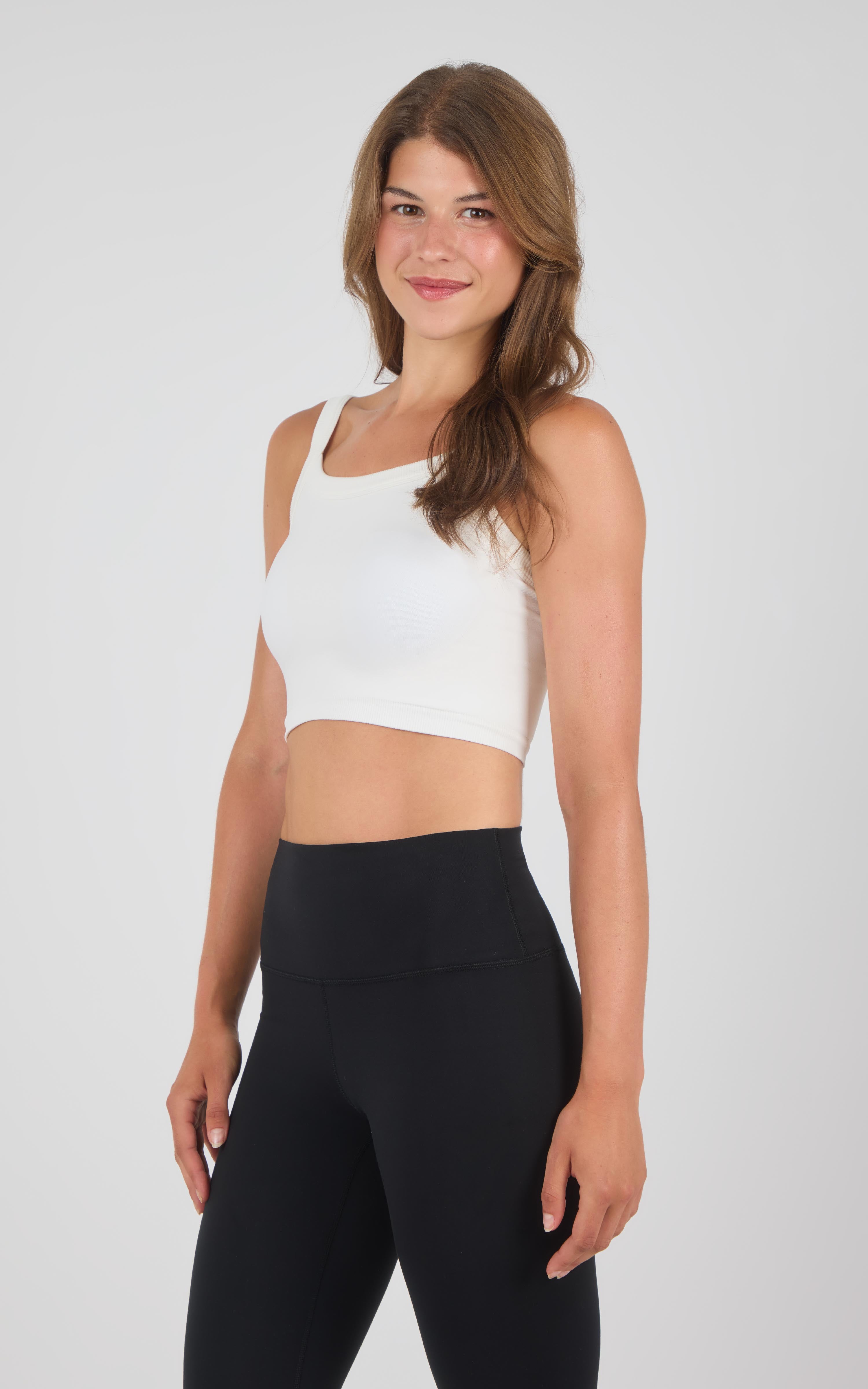 White seamless cropped tank top with wide straps worn with high-waist black leggings.