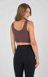 Seamless brown sports bra with wide straps and scoop back on woman in black leggings.