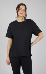 Woman wearing a black boxy short-sleeve top with a relaxed fit and curved hi-low hem, paired with black leggings.