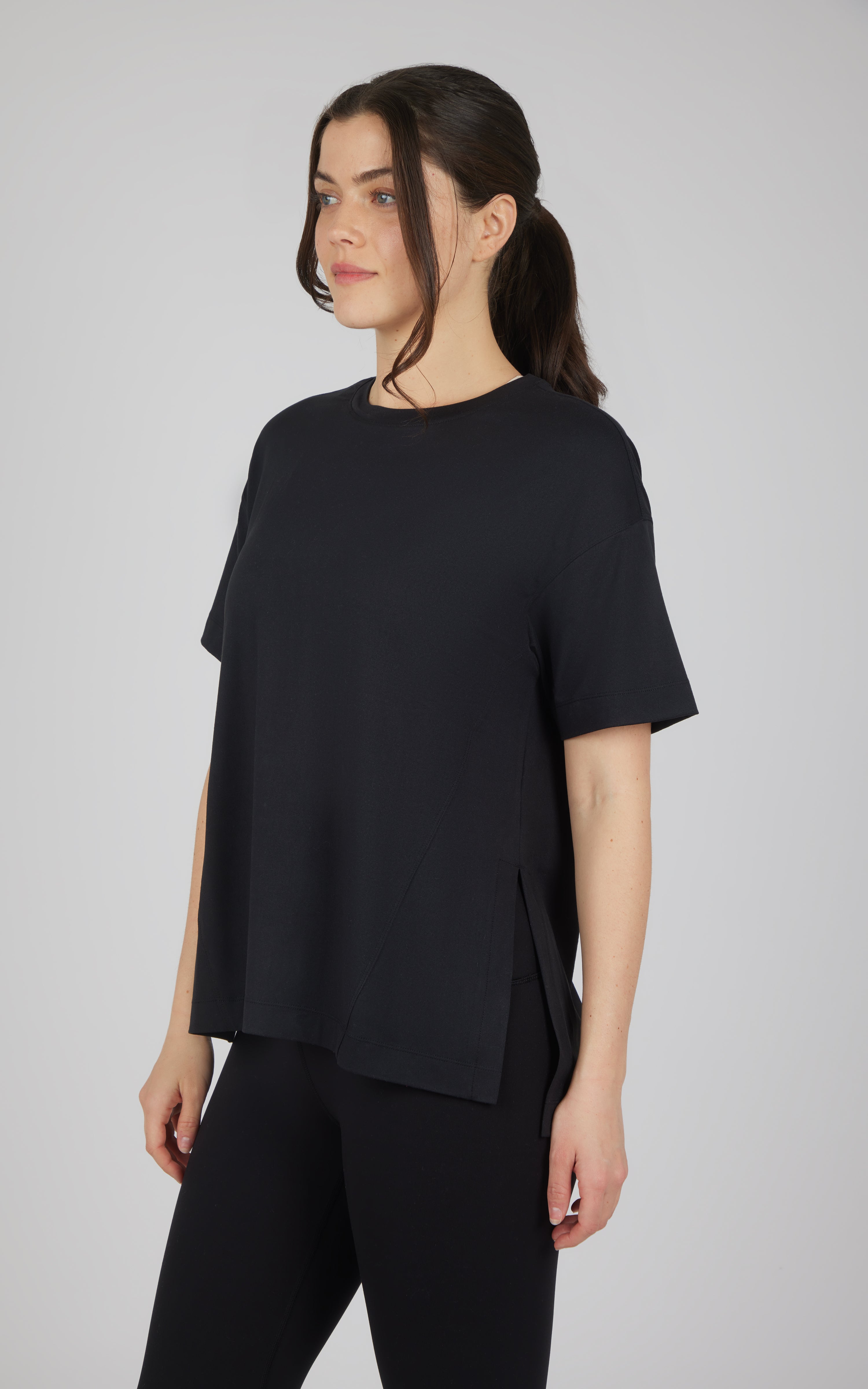 Model wearing a black boxy short-sleeve top with a high-low hem and black pants.