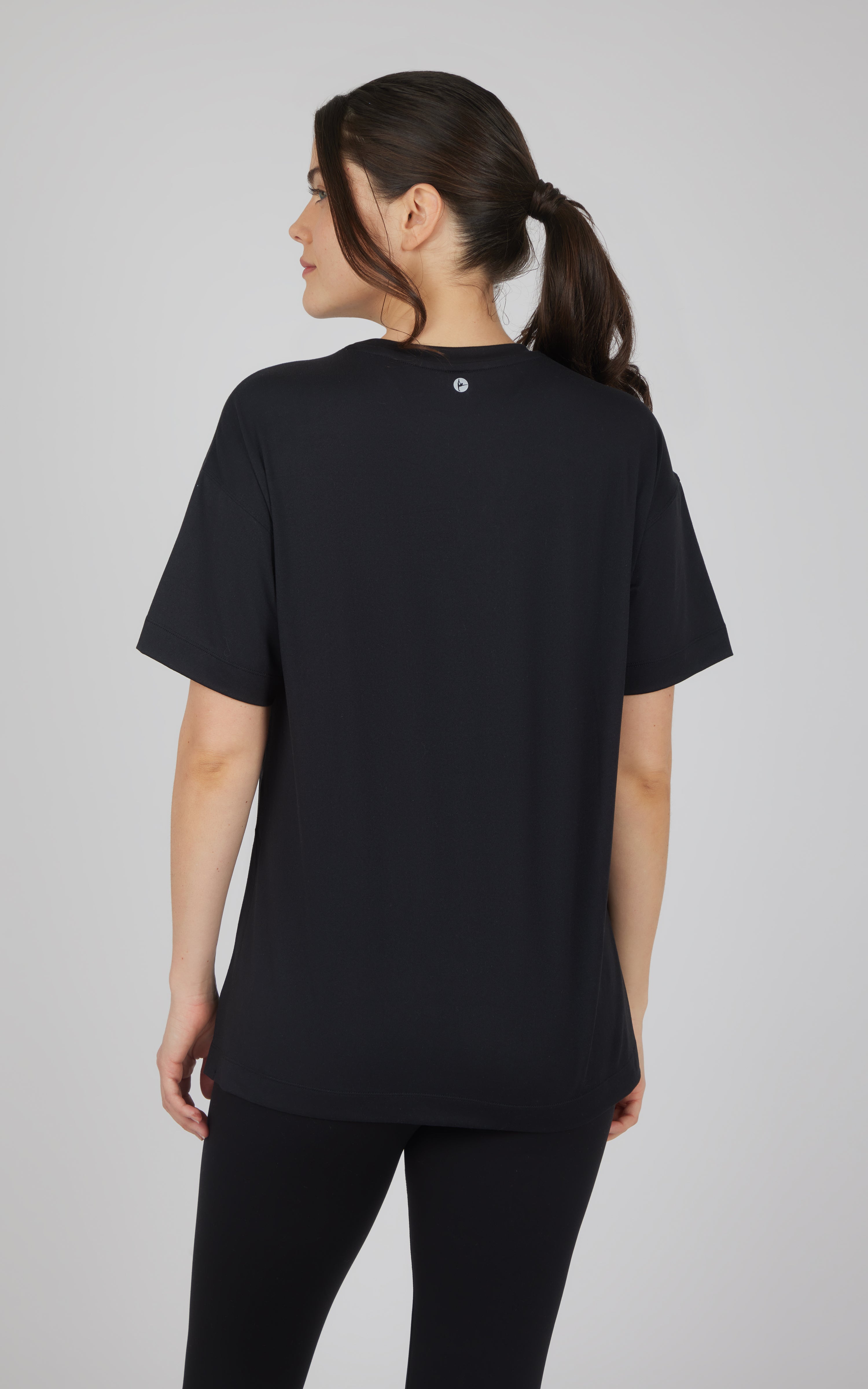 Black boxy short-sleeve top with a relaxed fit and high-low hem, shown from the back with black leggings.