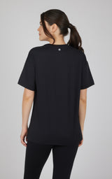 Black boxy short-sleeve top with a relaxed fit and high-low hem, shown from the back with black leggings.