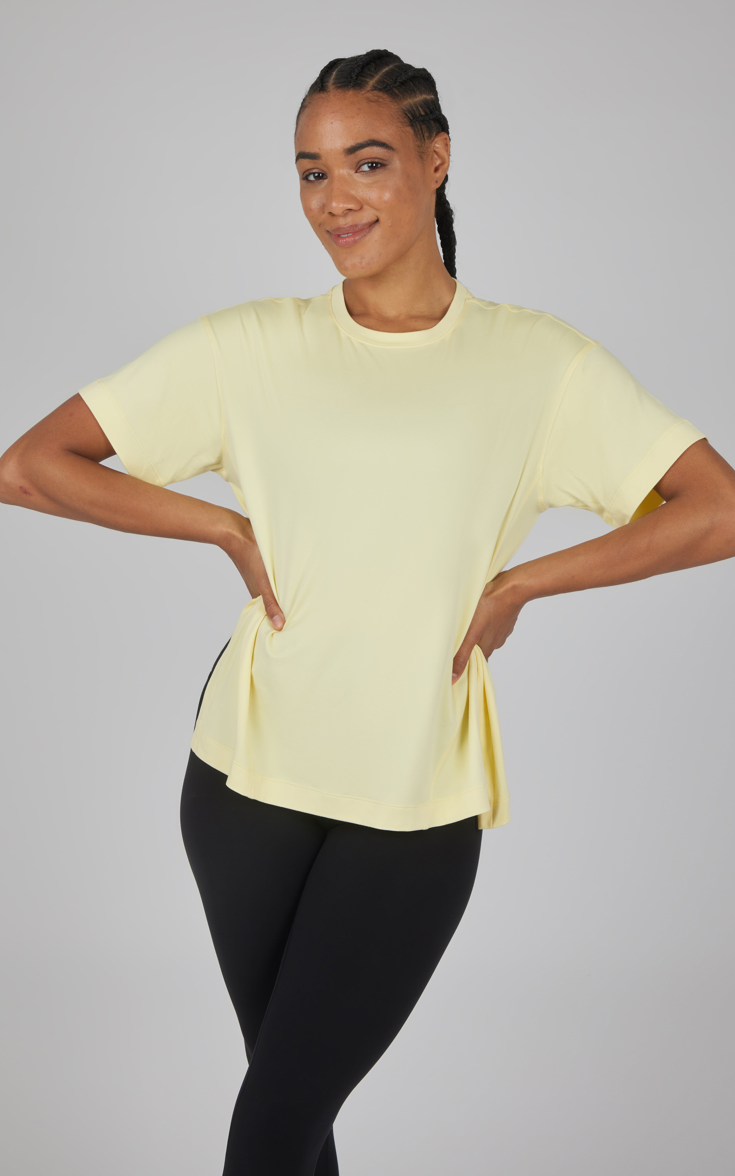 Woman modeling a pale yellow boxy short-sleeve top with a rounded neckline and curved hi-low hem.