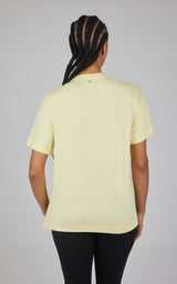 Back view of a pale yellow short-sleeve boxy top with a curved high-low hem, paired with black pants.