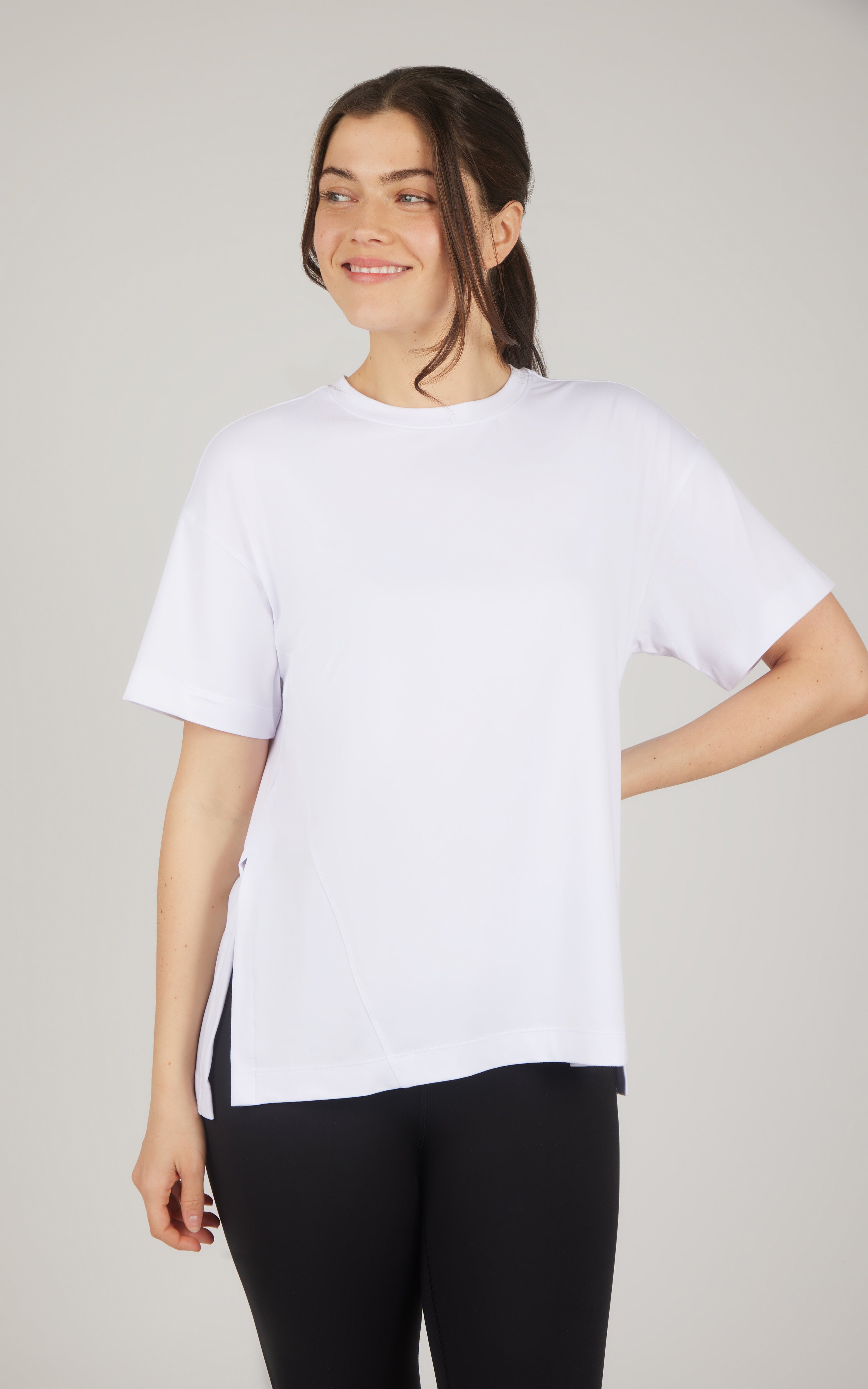 White boxy short-sleeve top with a relaxed fit, high-low hem, and soft draping, paired with black pants.