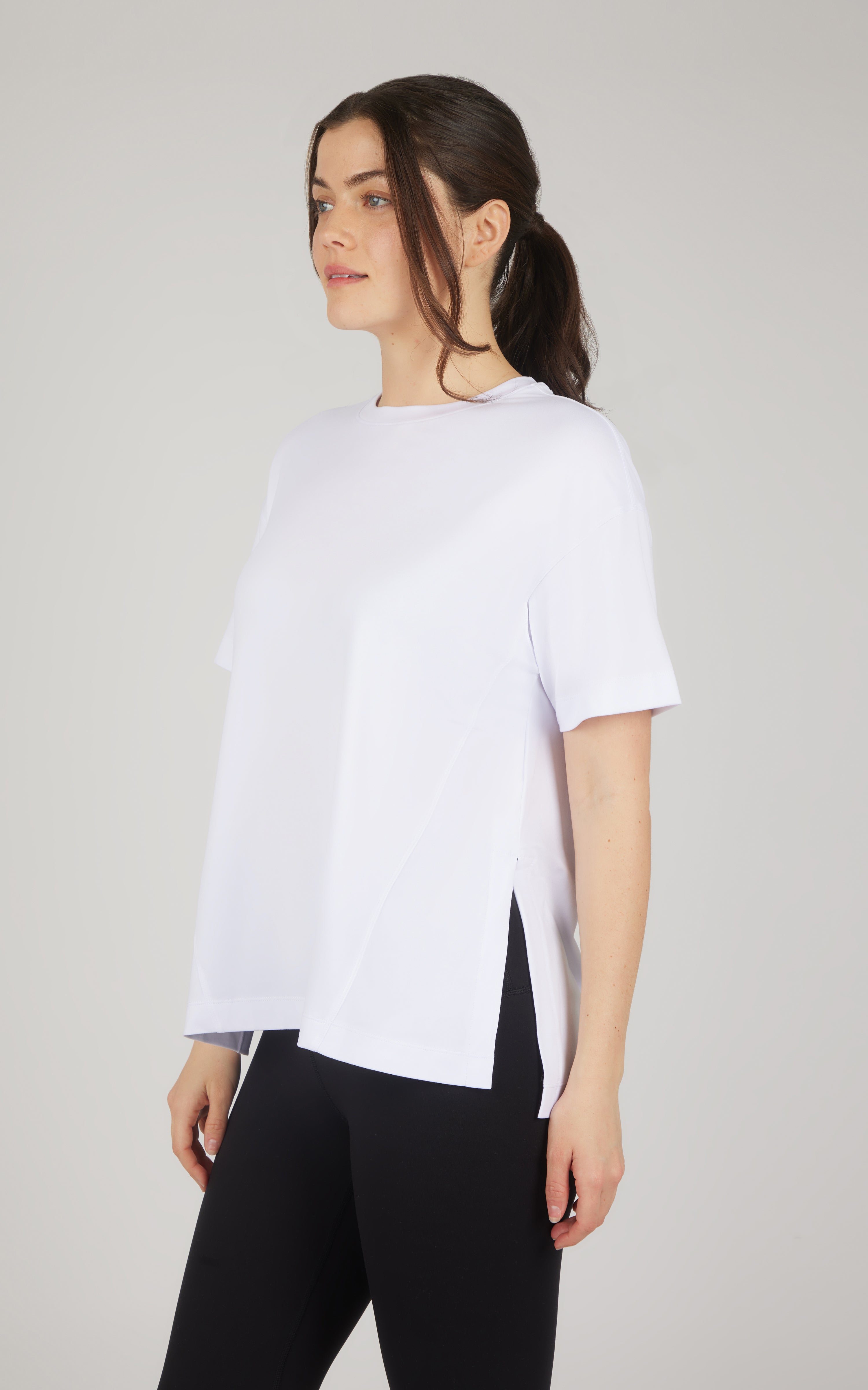 White boxy short-sleeve top with a rounded neckline and asymmetrical high-low hem, paired with black leggings.