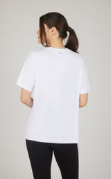 Back view of a white boxy short-sleeve top with a relaxed fit and slightly longer hem, paired with black leggings.