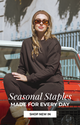 Model wearing a dark brown matching lounge set and shearling boots, sitting on the hood of a red vintage SUV. Text reads “Seasonal Staples, Made for Every Day” with a “Shop New In” button.