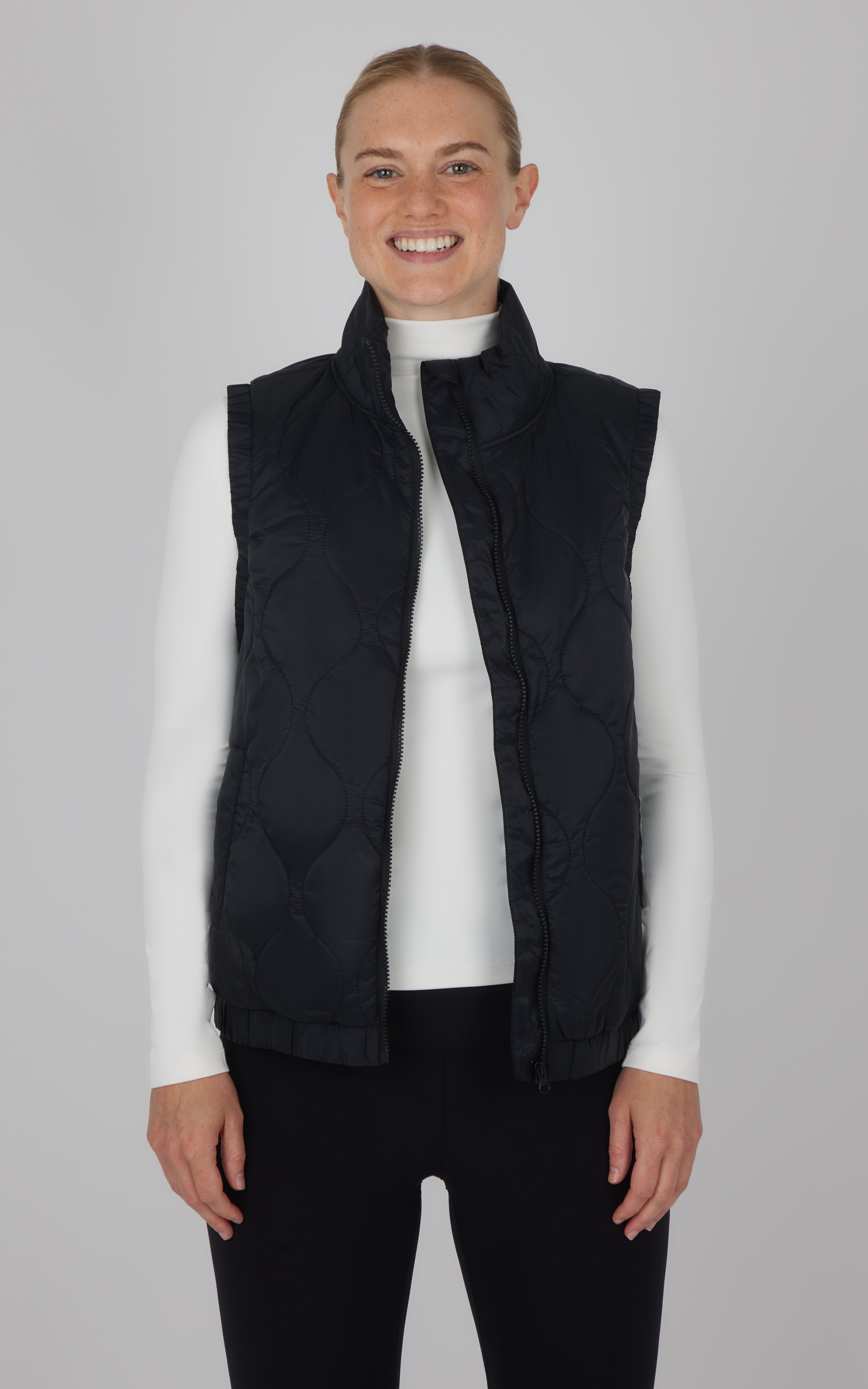 Black quilted sleeveless vest with high collar, worn over white long-sleeve top.