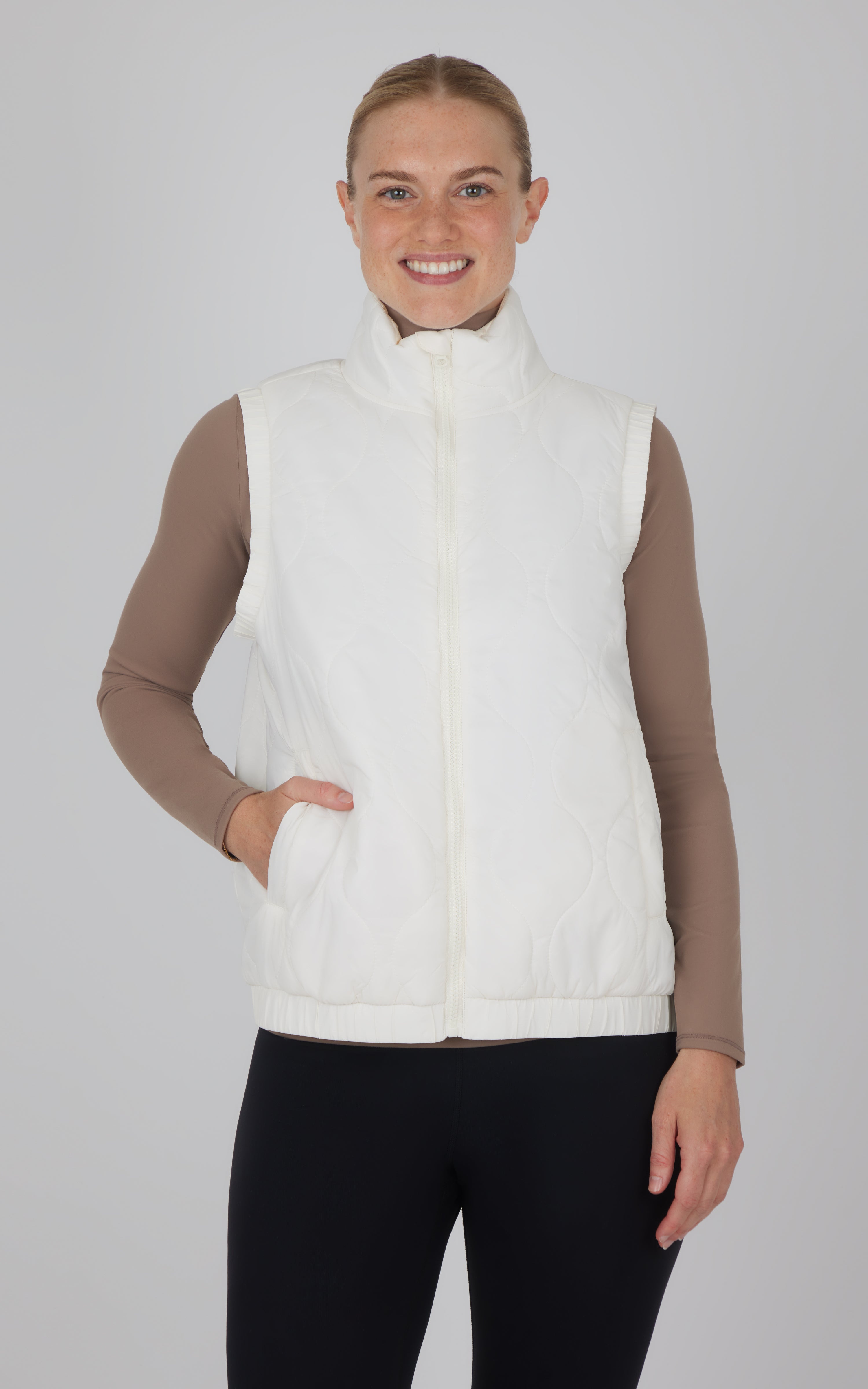 Cream-colored quilted vest with high collar and zip front, worn over beige long-sleeve shirt.
