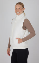White quilted sleeveless vest with high collar and side pockets, worn over a taupe long-sleeve top.