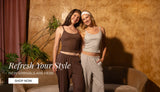 Two women posing in matching lounge sets in a warmly lit room with a textured gold wall, a curved sofa, and a potted plant. One set is dark brown and the other is light gray. Promotional text reads: "Refresh your style. new arrivals are here. shop now"