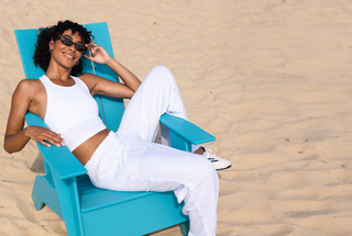 Woman in a white swimsuit and sunglasses sitting on a blue chair on sand