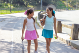 Two young girls with tennis rackets and balls on a road.