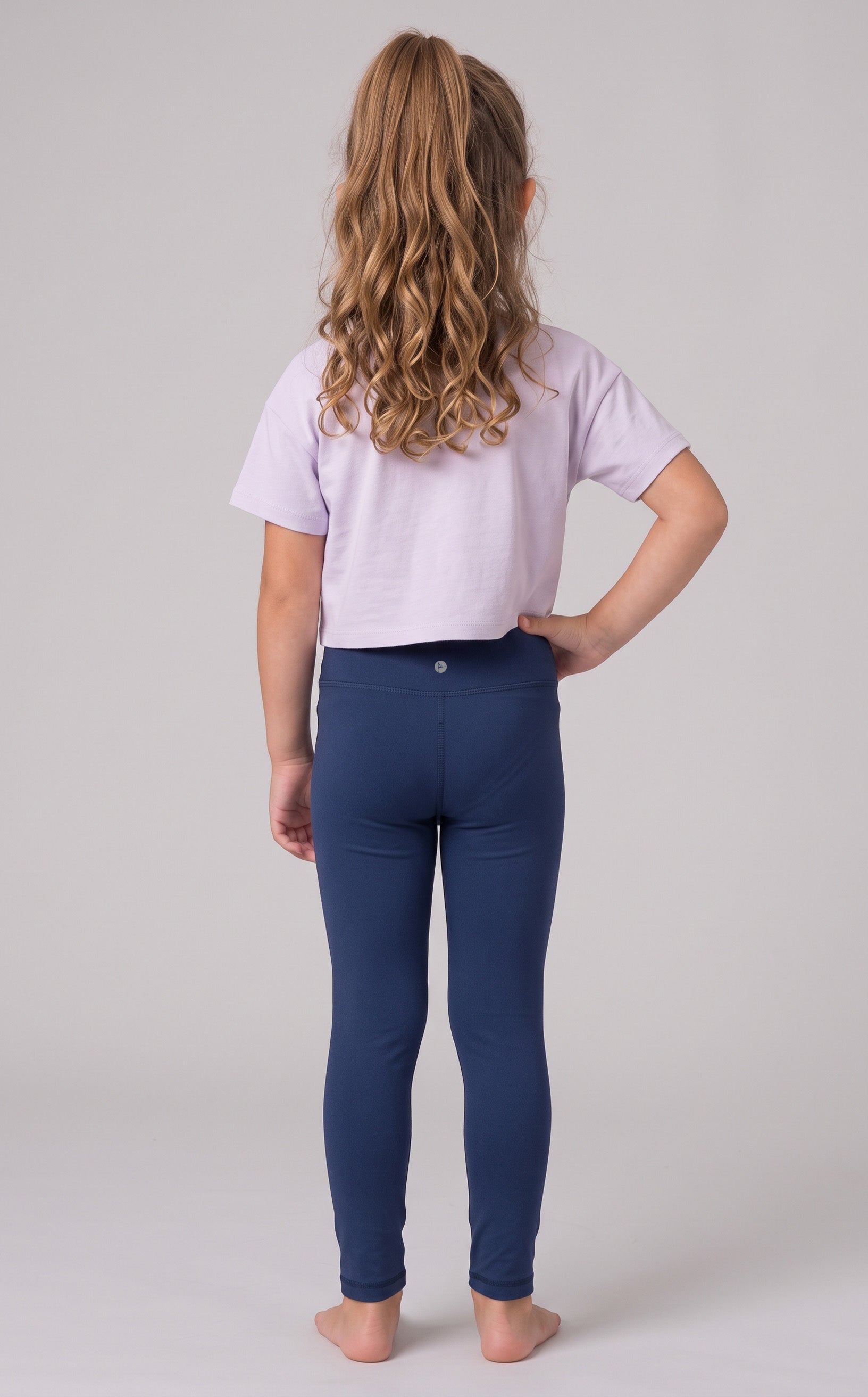Back view of a girl wearing full-length navy leggings with a smooth, stretchy fit and a lavender top.